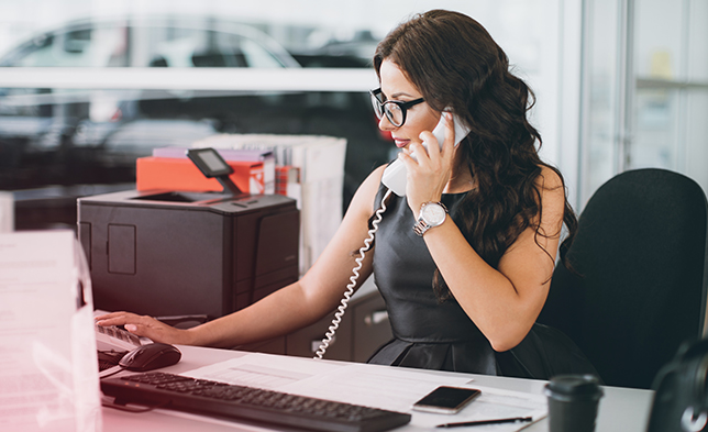 Woman using the phone while sitting at her desk in a dealership