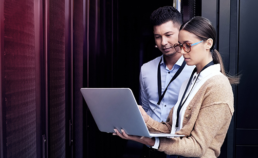 Two people looking over an incident report on a laptop in a server room