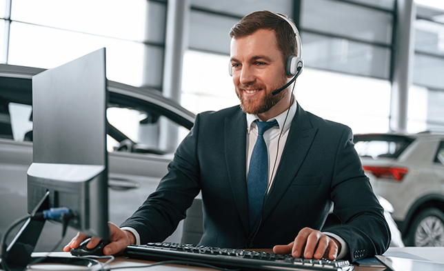 Dealership employee wearing a headset and on the computer while smiling